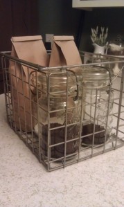 A small metal crate holds bags of fresh whole bean coffee and two antique Ball jars with locking lids with our ground coffee.  